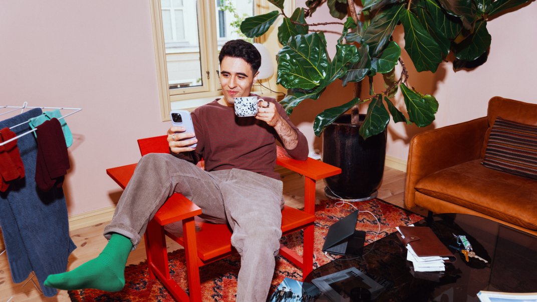 Kunde av Posten Bring sitter med mobiltelefon og kaffekopp