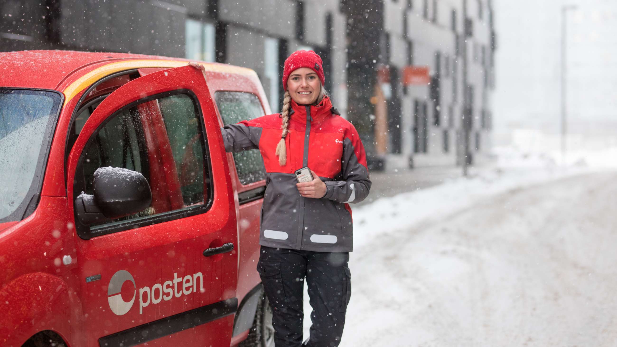 Kvinnelig postbud ved bil i snødekket gate