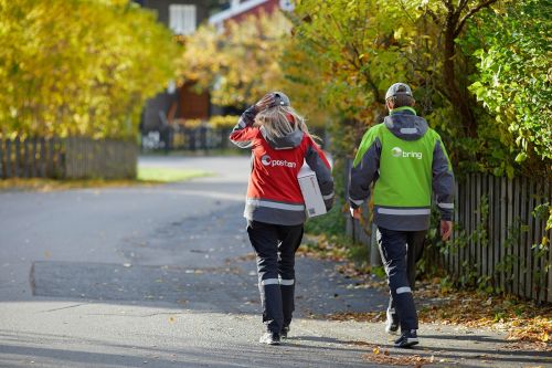 Kvinnelig postbud og mannlig Bring-bud går nedover veien.