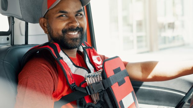 Smilende postbud sitter i førersetet i postbilen sin.