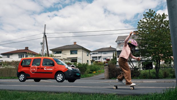 Barn skater på fortauet og en rød postbil i gata